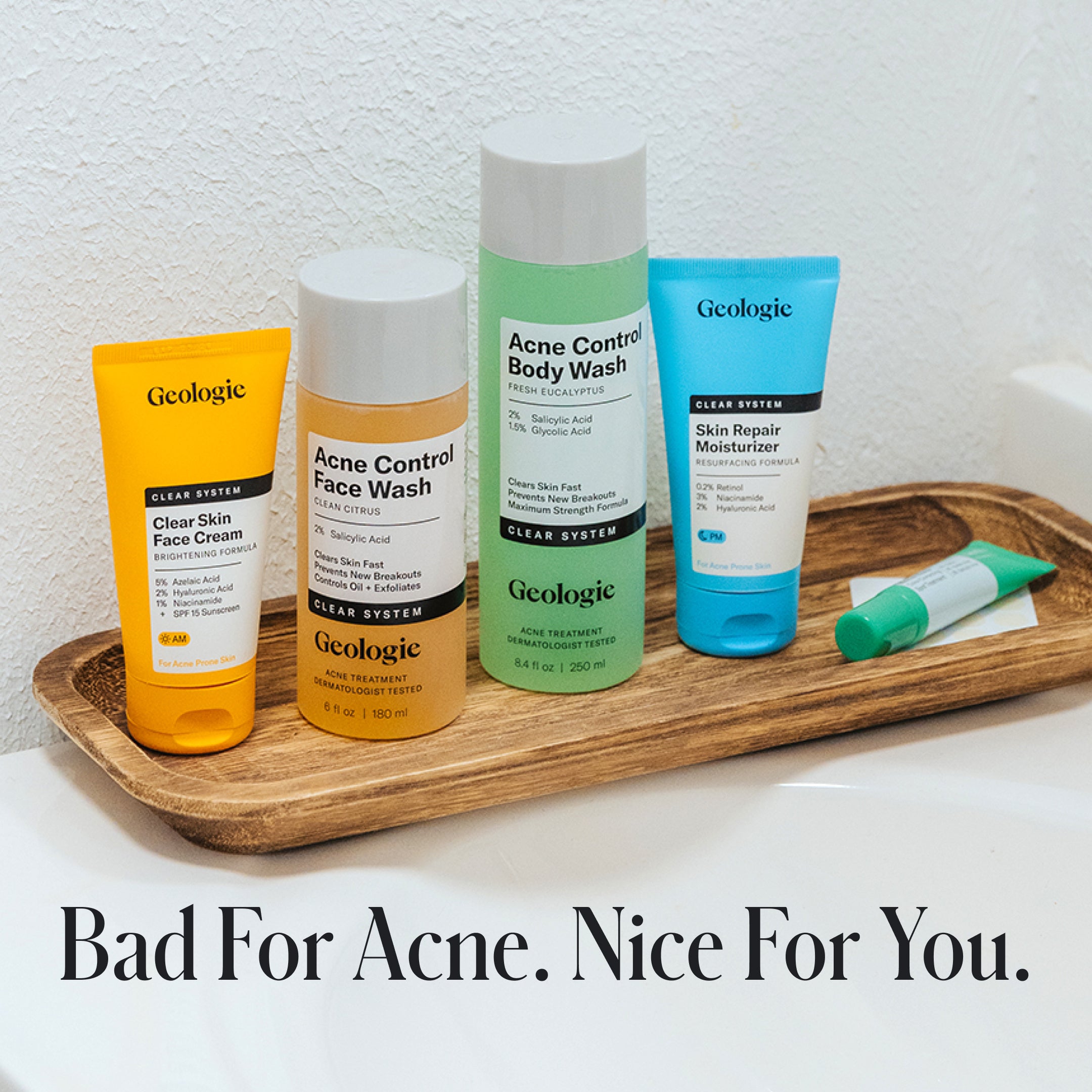 Four Geologie Skin Repair Moisturizer bottles are arranged on a wooden tray with the text, Bad For Acne. Nice For You. The display highlights hyaluronic acid for healthy, clear skin.