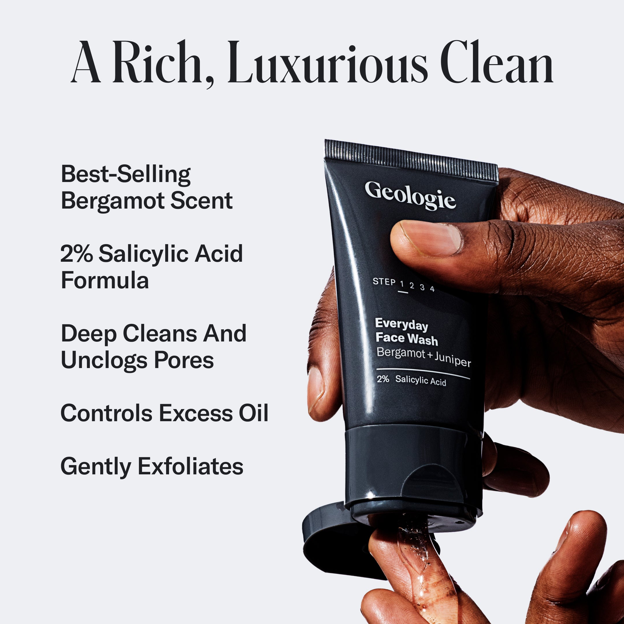 A hand holding a tube of Geologie Luxury Skincare Set face wash, with text describing its benefits like containing 2% salicylic acid and controlling excess oil.